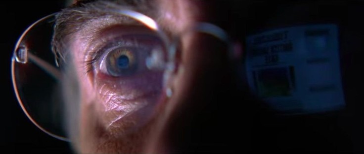 A close-up of a man’s hazel eye as he looks at a computer screen, editing a newspaper headline