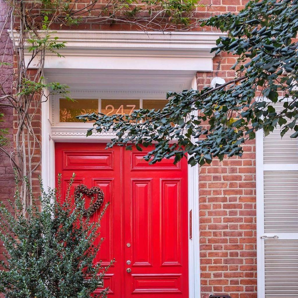 A vibrant red double door at number 247, adorned with a woven heart wreath and framed by lush green vines on a red brick townhouse.
