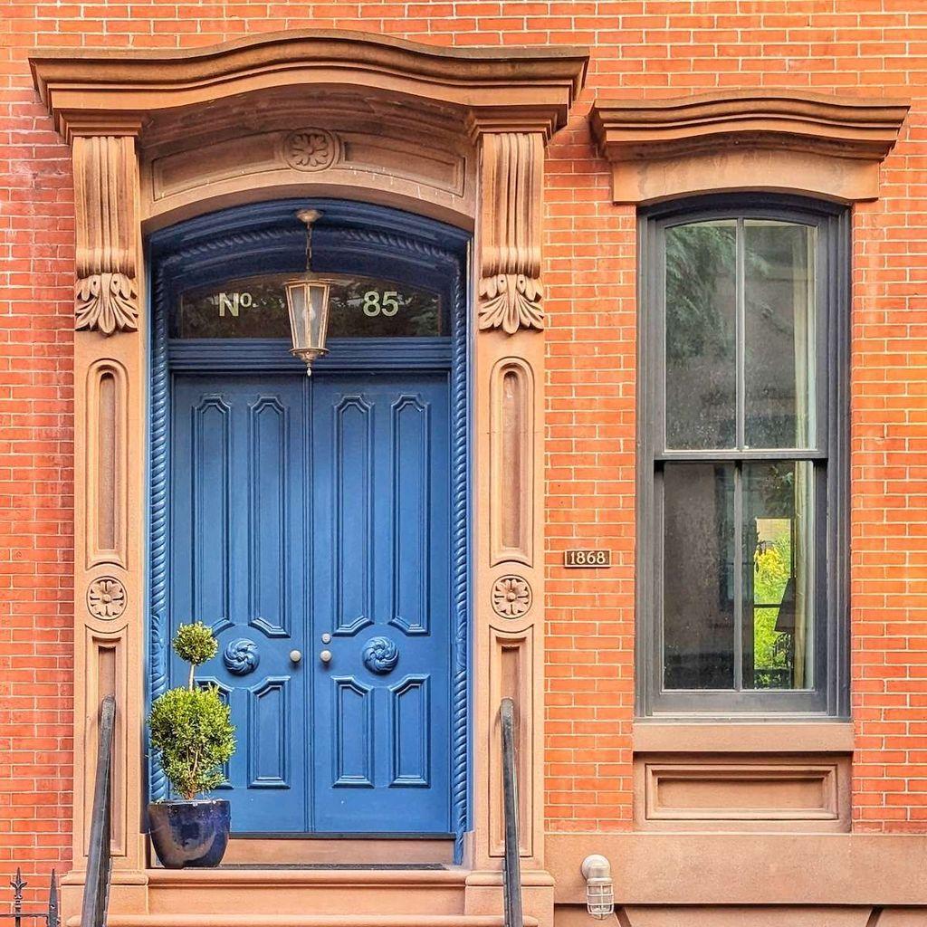 A sophisticated cobalt blue double door at number 85, featuring an ornate brownstone pediment and a hanging glass lantern.