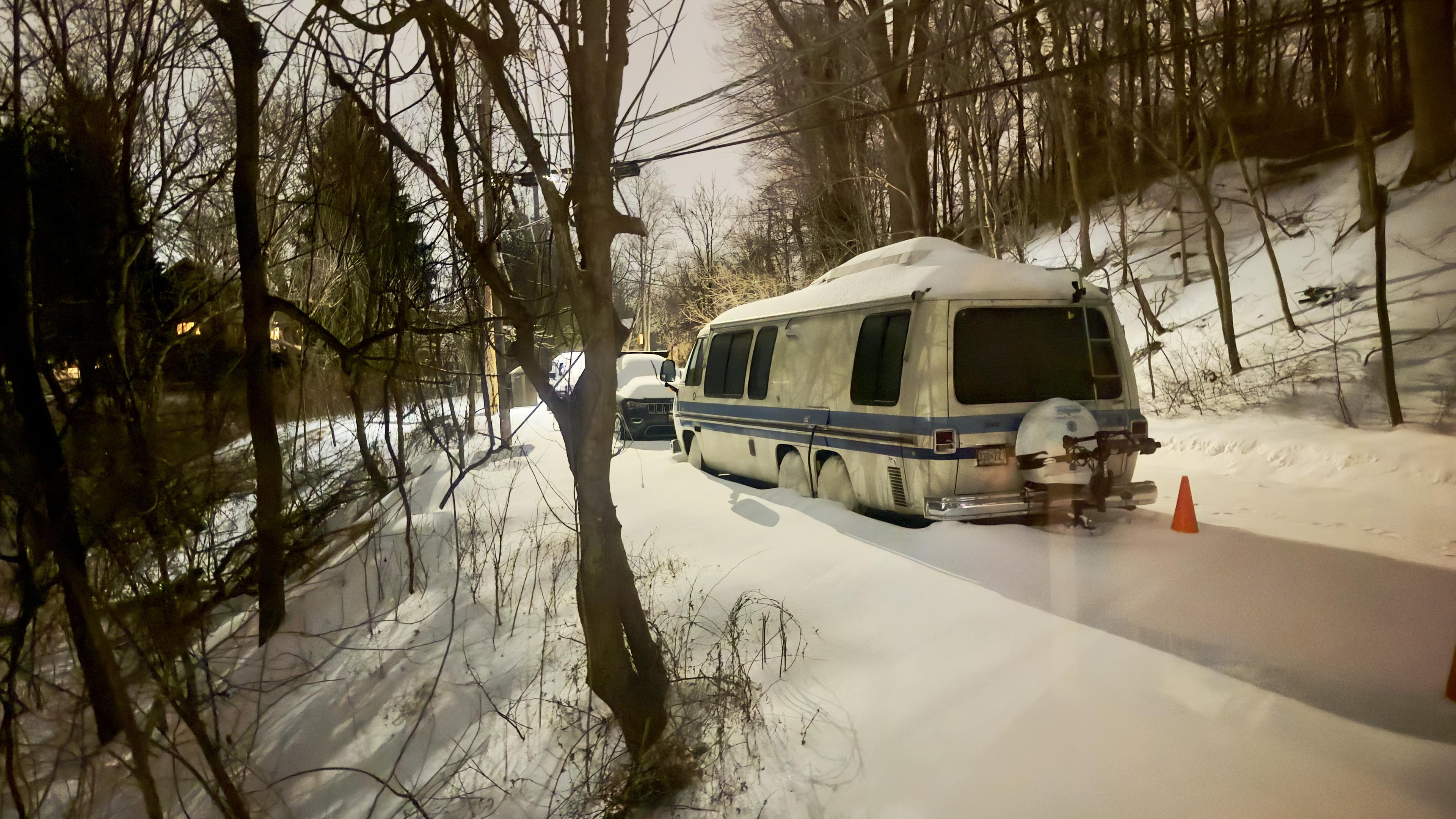A GMC Motorhome parked along a street in the woods surrounded by snowfall.