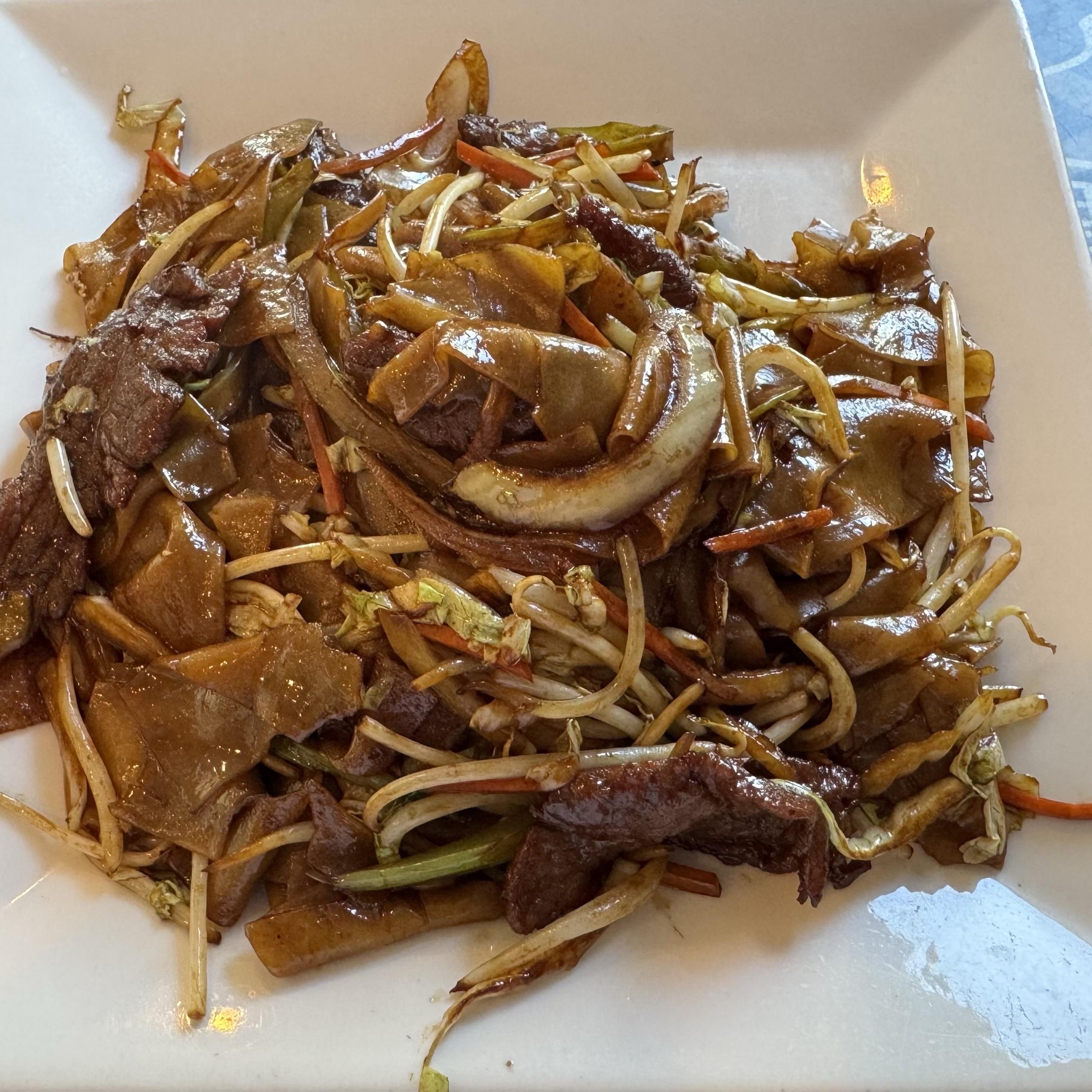 A plate of stir-fried beef and flat rice noodles, mixed with shredded vegetables and bean sprouts, presented on a white dish.