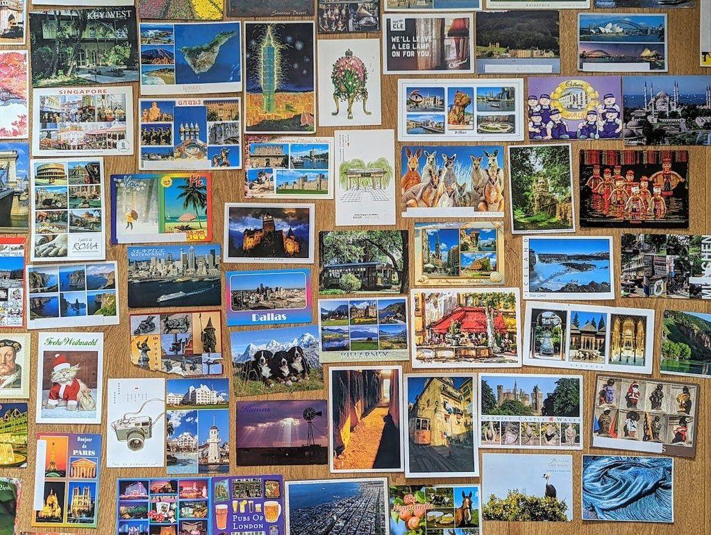 A flat lay image showing a large, colorful collection of various vintage travel postcards from around the world, serving as postcard examples.